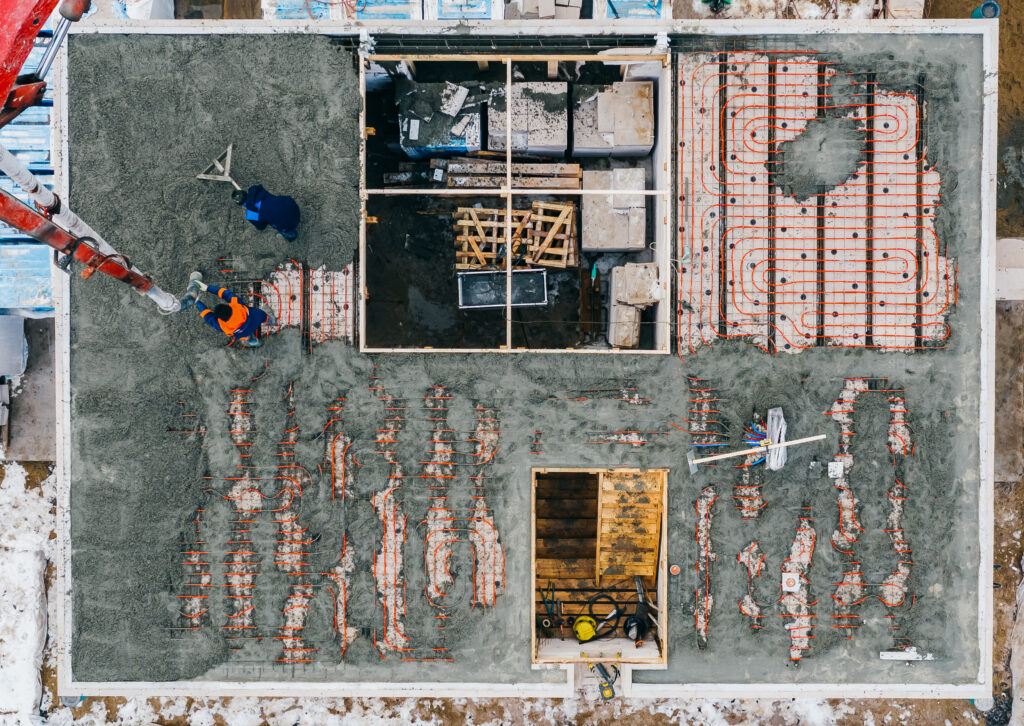 Aerial view of construction workers pouring a wet concrete at floor heating system installation in new house construction site