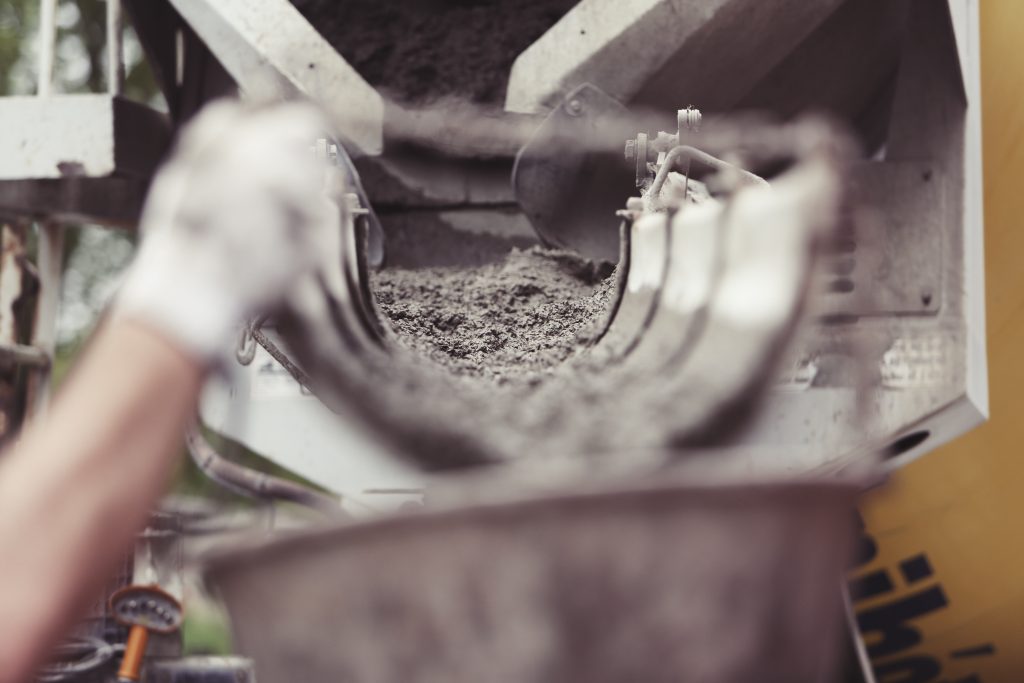 A hand holds a chute to pour some ready mix concrete on a hot summer day.